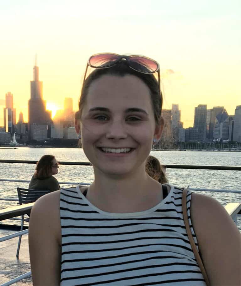 Woman smiling at sunset, city skyline in background.